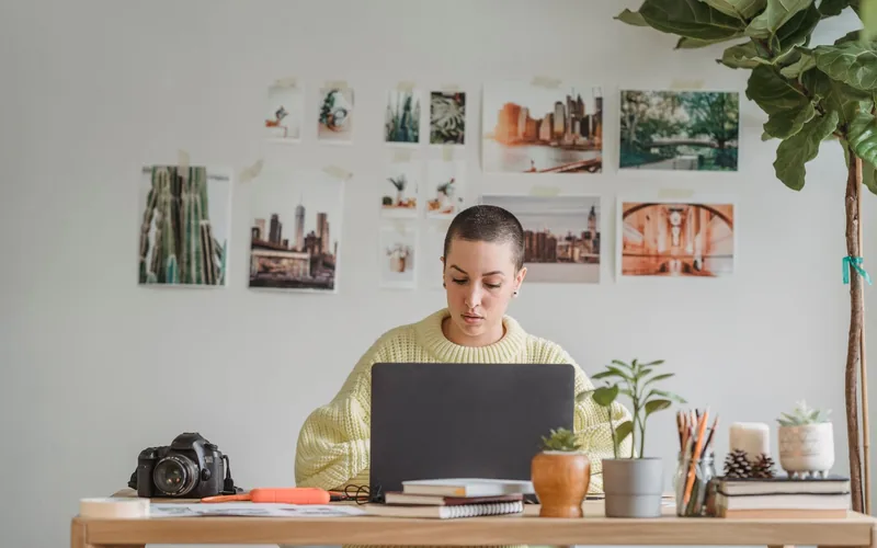 Kobieta pracuje przy laptopie w jasnym miejscu pracy; fotografia ilustracyjna.